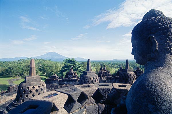 Buddha statue atop Borobudur, with Mount Merapi in background, Java